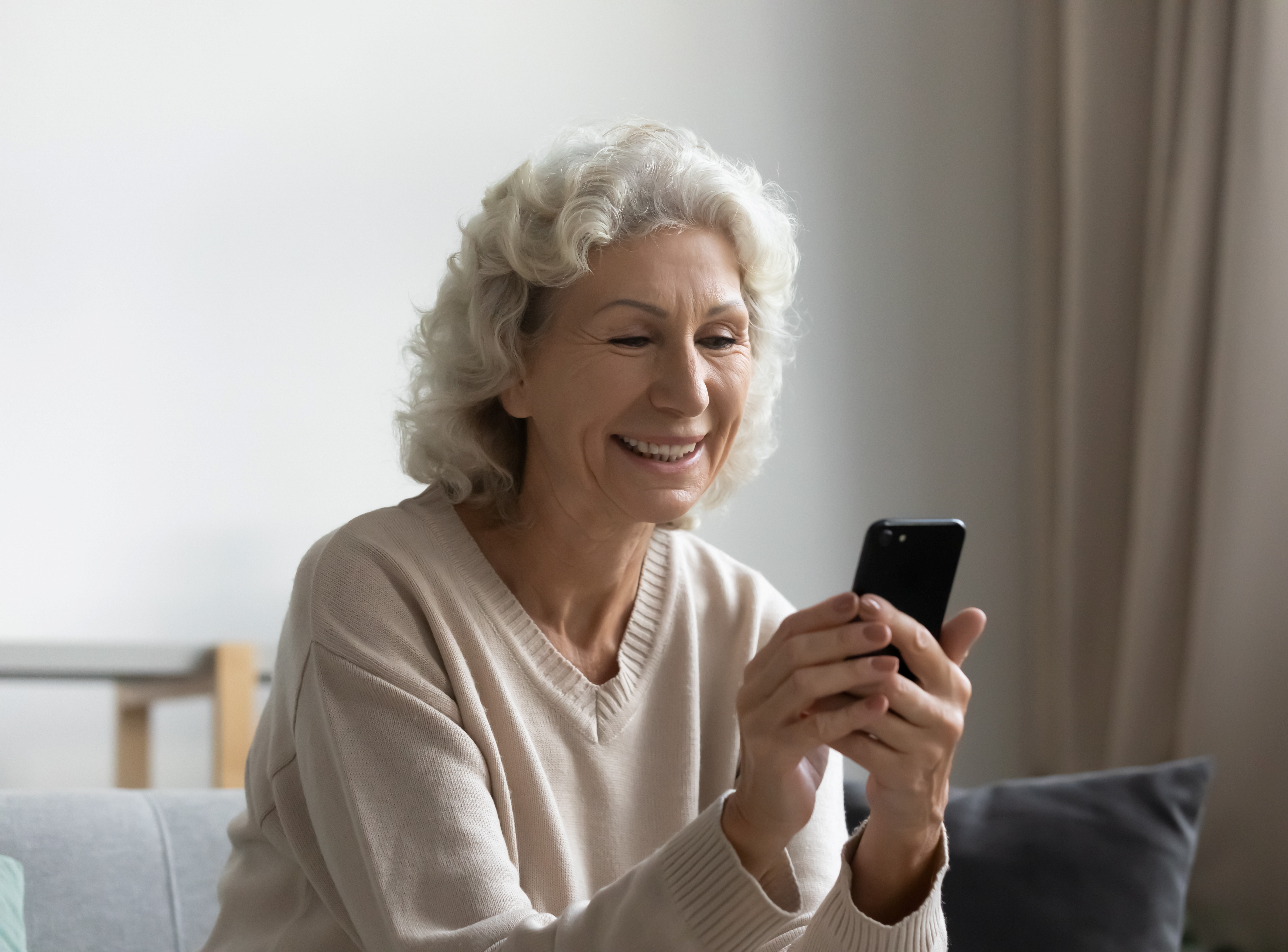 Senior woman with white hair smiling while using phone